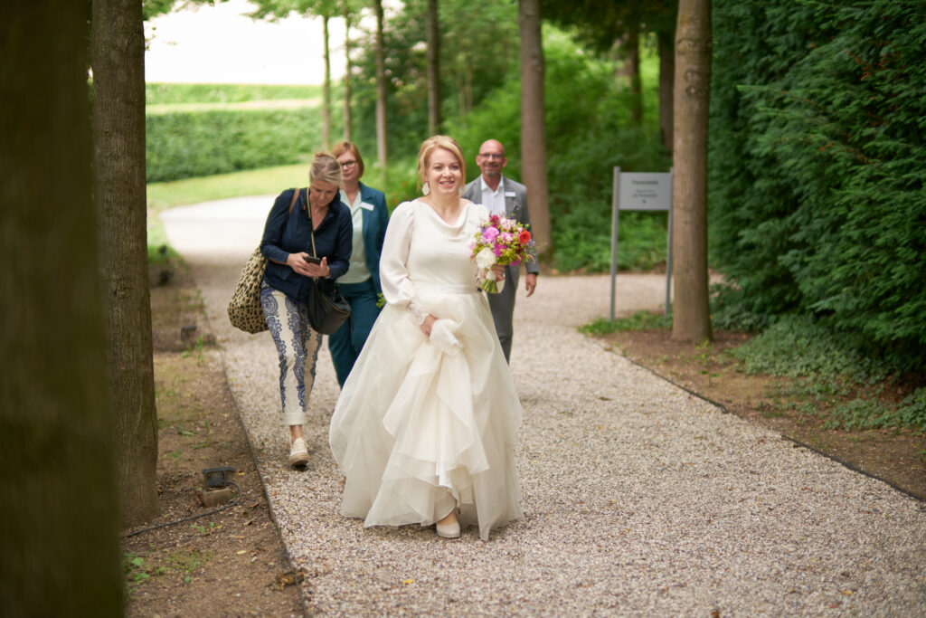 Braut im weißen Brautkleid kommt in Begleitung von Trauzeugin und Weddingplanner durch Garten im Stift Melk